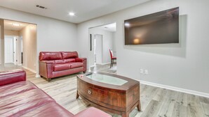 A spacious living room with a red leather sofa, a glass-top coffee table, and a large painting on the wall. - Pensacola Home w/ Private Yard: 7 Mi to Downtown! (Pensacola)