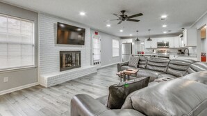 A modern living room with a fireplace, leather sofa, and a kitchen area in the background. - Pensacola Home w/ Private Yard: 7 Mi to Downtown! (Pensacola)