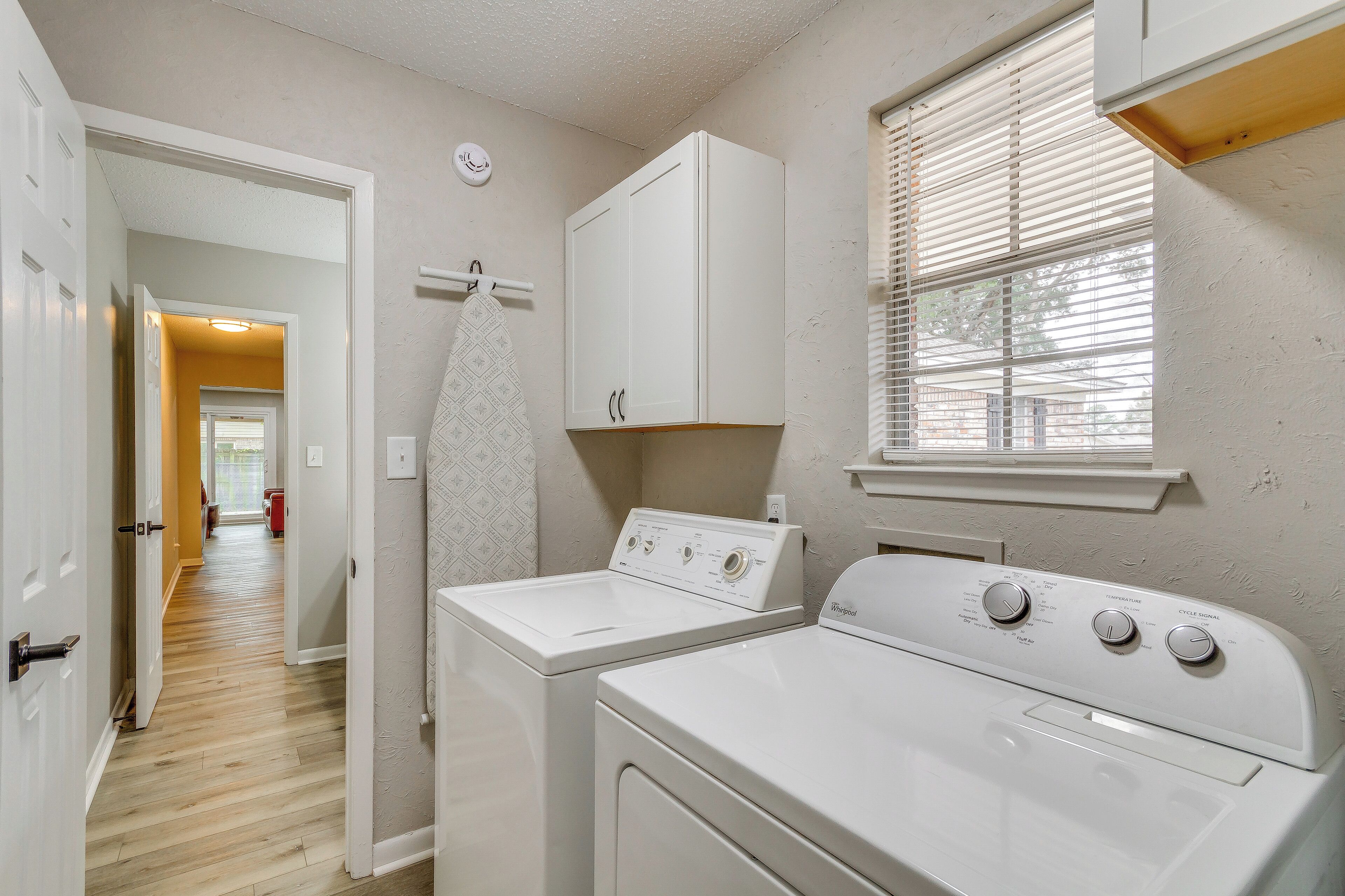 A laundry area with two white washers and dryers, a wooden floor, and a window with blinds.