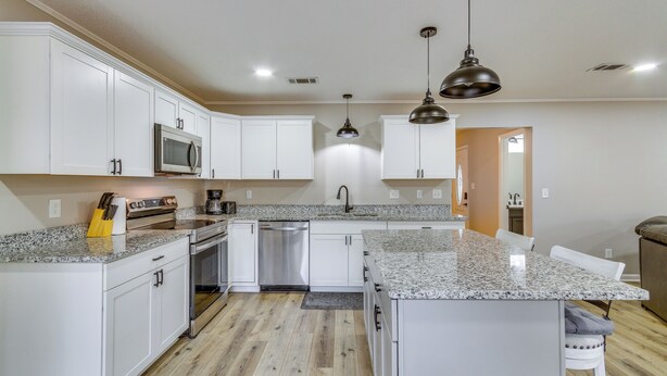 A modern kitchen with white cabinets, granite countertops, stainless steel appliances, and pendant lighting. - Pensacola Home w/ Private Yard: 7 Mi to Downtown! (Pensacola)