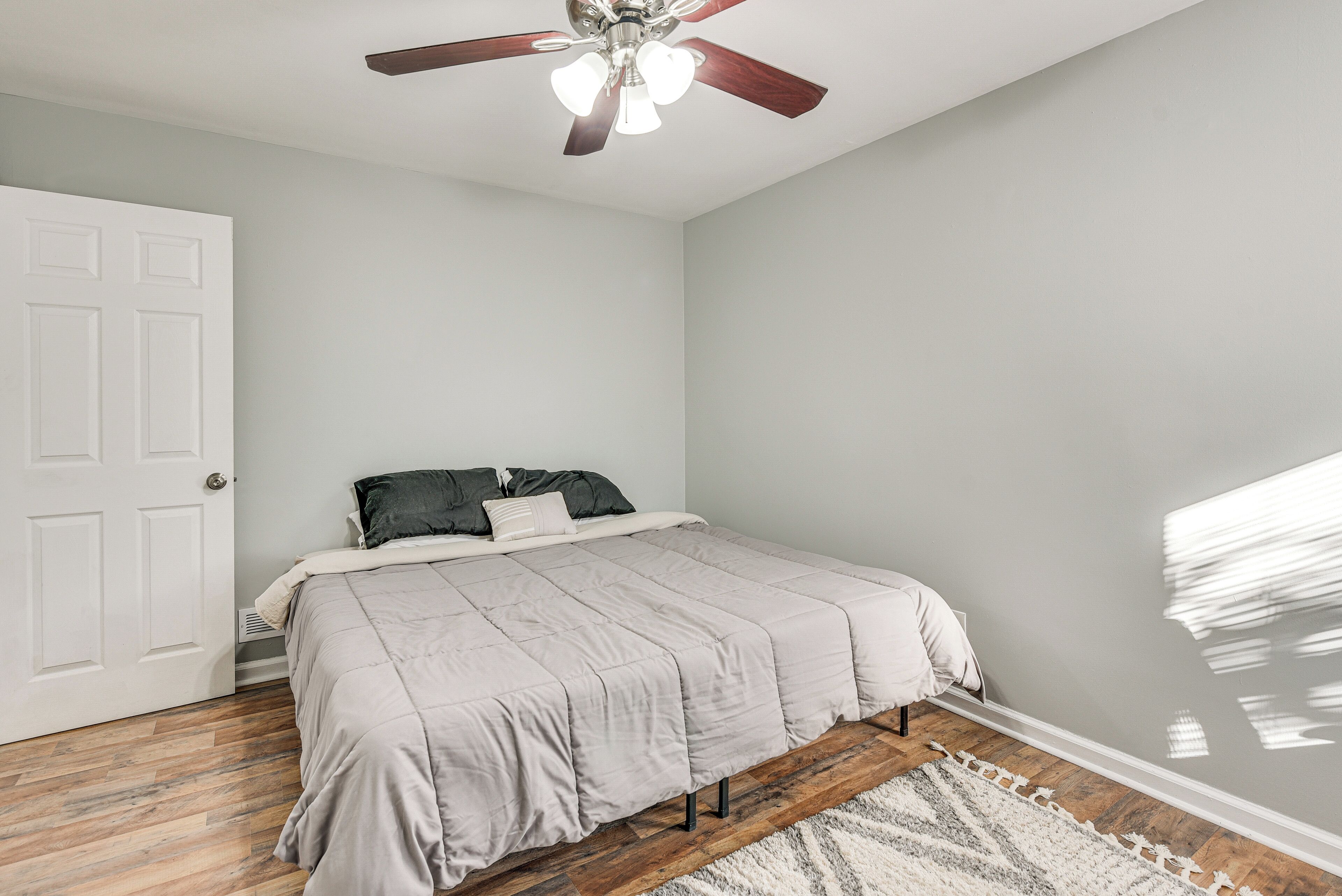 A bedroom with a bed, a ceiling fan, a white door, and a wooden floor.
