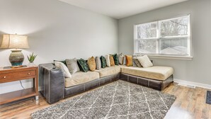 Un salon moderne avec un canapé d’angle, une table d’appoint en bois et un tapis à motifs.