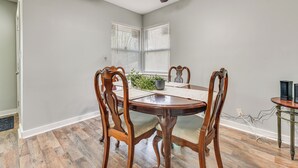Un coin repas avec une table et des chaises en bois, un ventilateur de plafond et une fenêtre avec des stores.
