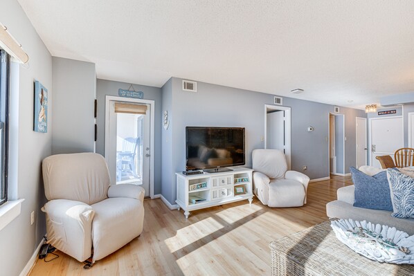 A spacious living room with a large flat-screen TV, comfortable seating, and a wooden floor.