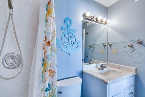 A bathroom with a shower, a toilet, a sink, and a mirror with lights. - Seaside Indian Beach Getaway w/ Balcony + Views! (Atlantic Beach)