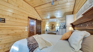 A wooden cabin bedroom with a bed, pillows, a headboard, a ceiling fan, and a small kitchenette area. - Hook, Line, & Sinker Retreat: Fire Pit, Grill! (Broken Bow)
