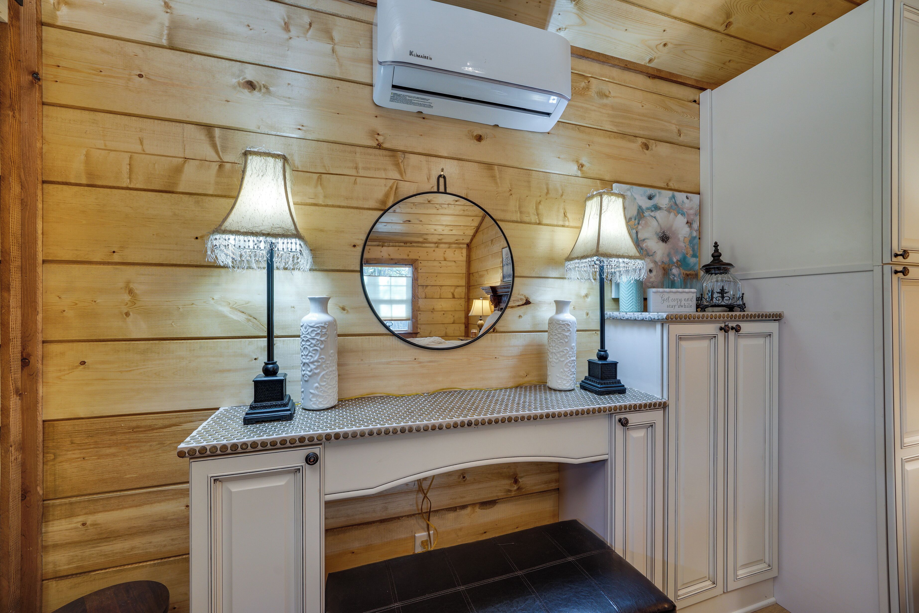 Une salle de bain aux murs lambrissés, équipée d’un meuble-lavabo, de deux lampes, d’un miroir et d’un appareil de climatisation.