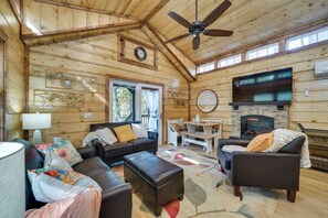 A cozy cabin interior with a fireplace, wooden walls, a ceiling fan, and a dining area. - Hook, Line, & Sinker Retreat: Fire Pit, Grill! (Broken Bow)