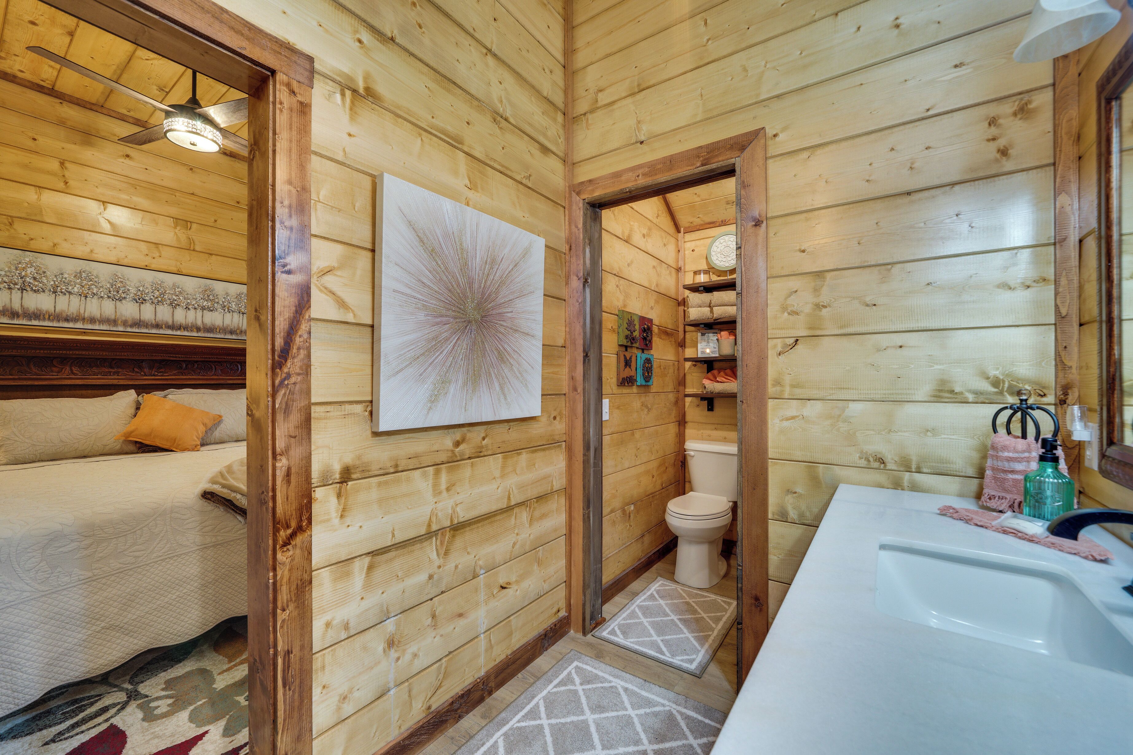 A wooden cabin interior with a bed, a bathroom, and a ceiling fan.
