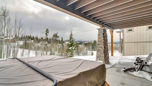 Une terrasse couverte équipée d’un barbecue, agrémentée de piliers en pierre et offrant une vue sur un paysage enneigé.