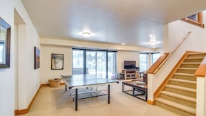Un grand espace de vie comprenant une table de ping-pong, un téléviseur et un escalier.