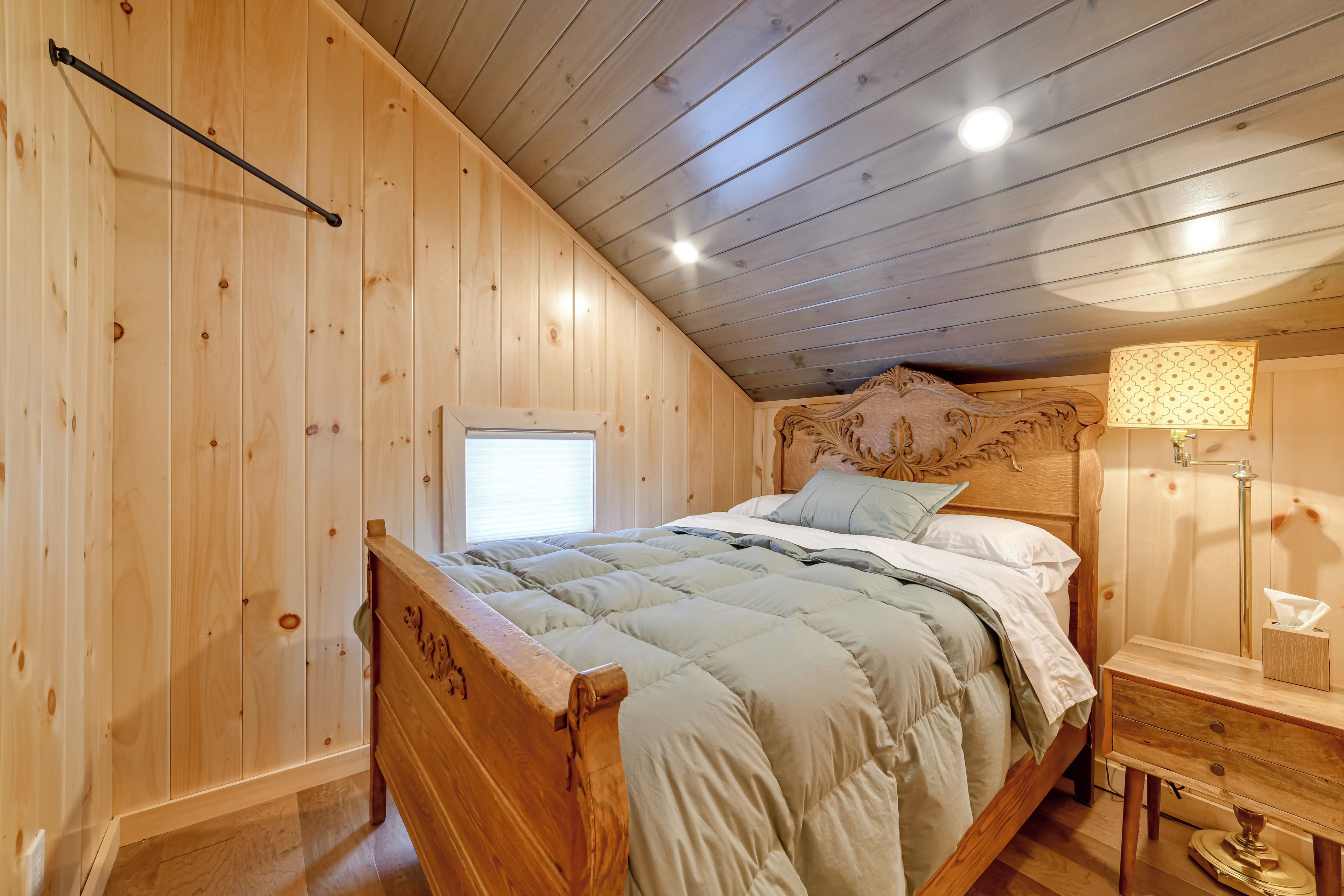 Une chambre à coucher aux murs lambrissés, avec un lit, une table de chevet, une lampe et une fenêtre.