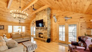 A log cabin interior with a stone fireplace, wooden ceiling beams, a television, and leather sofas. - W Branch Del Cabin Fully Equipped: Private Island (Deposit)