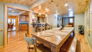 A spacious dining area with a long wooden table, surrounded by chairs, and a kitchen area with wooden cabinets and a stone countertop. - W Branch Del Cabin Fully Equipped: Private Island (Deposit)