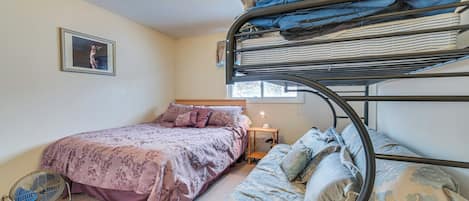 A bunk bed room with a single bed, a bedside table with a lamp, and a fan.