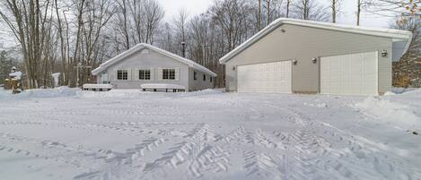 A two-story house with a garage, surrounded by snow-covered ground and leafless trees.