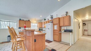 A modern kitchen with wooden cabinets, a central island with bar stools, a refrigerator, and a microwave. - Secluded Mancelona Home w/ Gas Grill! (Mancelona)