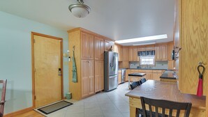A kitchen with wooden cabinets, a refrigerator, a dining table with chairs, and a window with curtains. - Large Home w/ Deck & Grill ~ 9 Mi to Virginia Tech (Christiansburg)