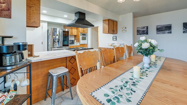 A modern kitchen with a central island, wooden chairs, and a dining table with a floral table runner. - Family-friendly Winston Vacation Rental w/ Deck! (Winston)