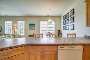 A kitchen with a granite countertop, wooden cabinets, a dishwasher, and a dining area with chairs and a table. - 4 Mi to Beaches: Pet-friendly Lewes Condo! (Lewes)