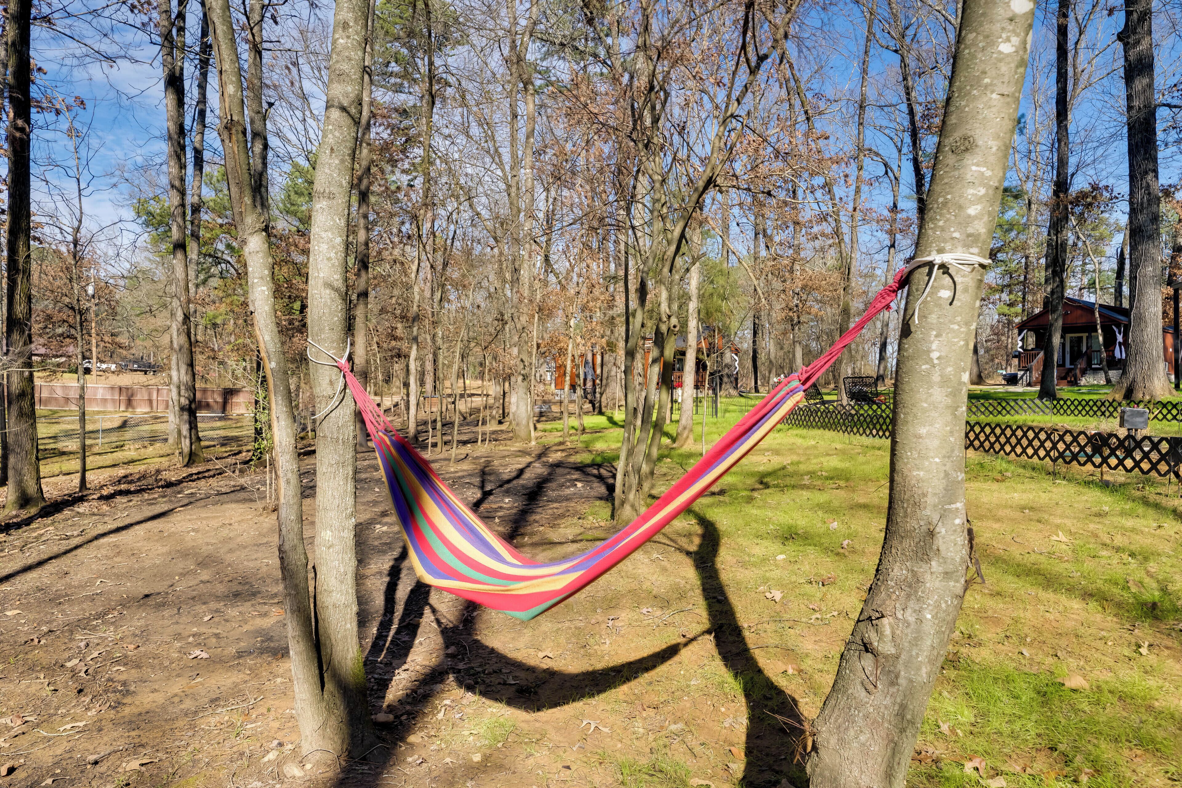 Een hangmat gespannen tussen bomen in een park, met een houten blokhut op de achtergrond.