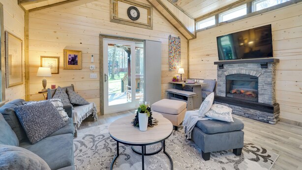 A cozy living room with a fireplace, wooden walls, and a large TV. - 'sweet Spot' Cabin in Broken Bow w/ Fire Pit! (Broken Bow)