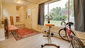 Una habitación con suelo de madera, un tapete rojo estampado, una bicicleta y una ventana con cortinas.