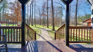 Une terrasse en bois avec un chemin de pierre menant à une zone herbeuse entourée d’arbres.