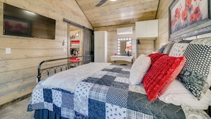Une chambre confortable avec un plafond en bois, un lit recouvert d’une courtepointe, un ventilateur de plafond et un miroir avec des lumières.