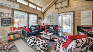 Un intérieur de chalet chaleureux avec un plafond en bois, un canapé en cuir noir, un coin bar et une vue sur l’extérieur.