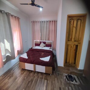 A bedroom with a bed, curtains, a wooden door, and a ceiling fan. - Hotel Silverine Srinagar (Srinagar)