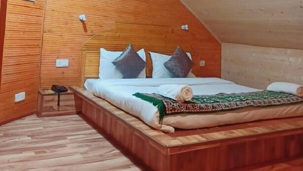 A cozy attic bedroom with a wooden sloped ceiling, a single bed with pillows, and a small bedside table. - Hotel Silverine Srinagar (Srinagar)