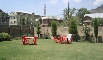 Un patio trasero con césped, una mesa y sillas, rodeado por un bajo muro de piedra y edificios residenciales al fondo.