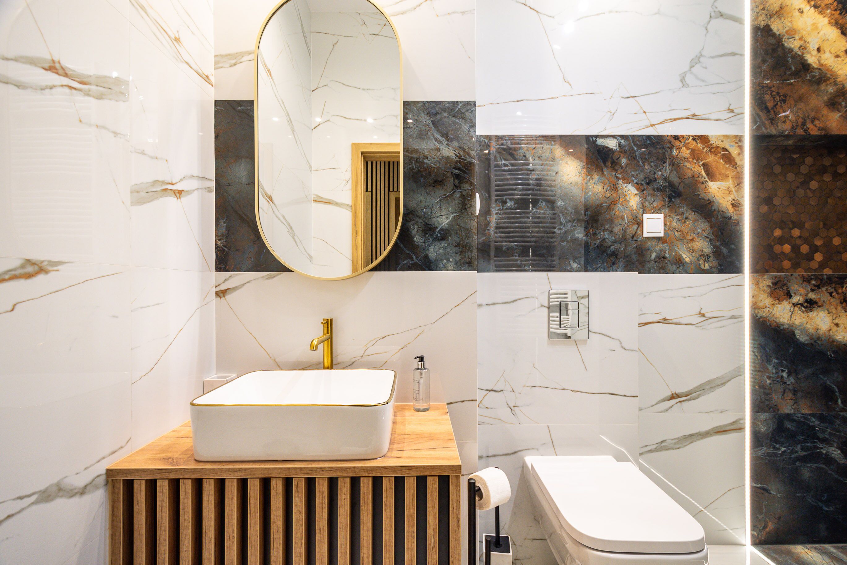 Un baño moderno con lavamanos blanco, grifo dorado y tocador de madera.