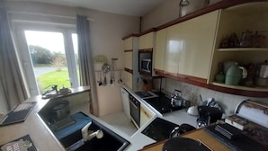 Une cuisine compacte équipée d’un évier, d’une cuisinière et d’un four à micro-ondes. Une fenêtre offre une vue sur la verdure environnante.
