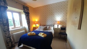 Une chambre à coucher avec un lit, deux tables de chevet, une fenêtre et un radiateur.