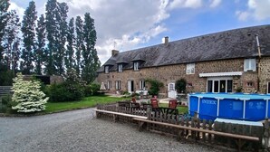 Un bâtiment en pierre avec une allée en gravier, une clôture en bois et une piscine bleue.