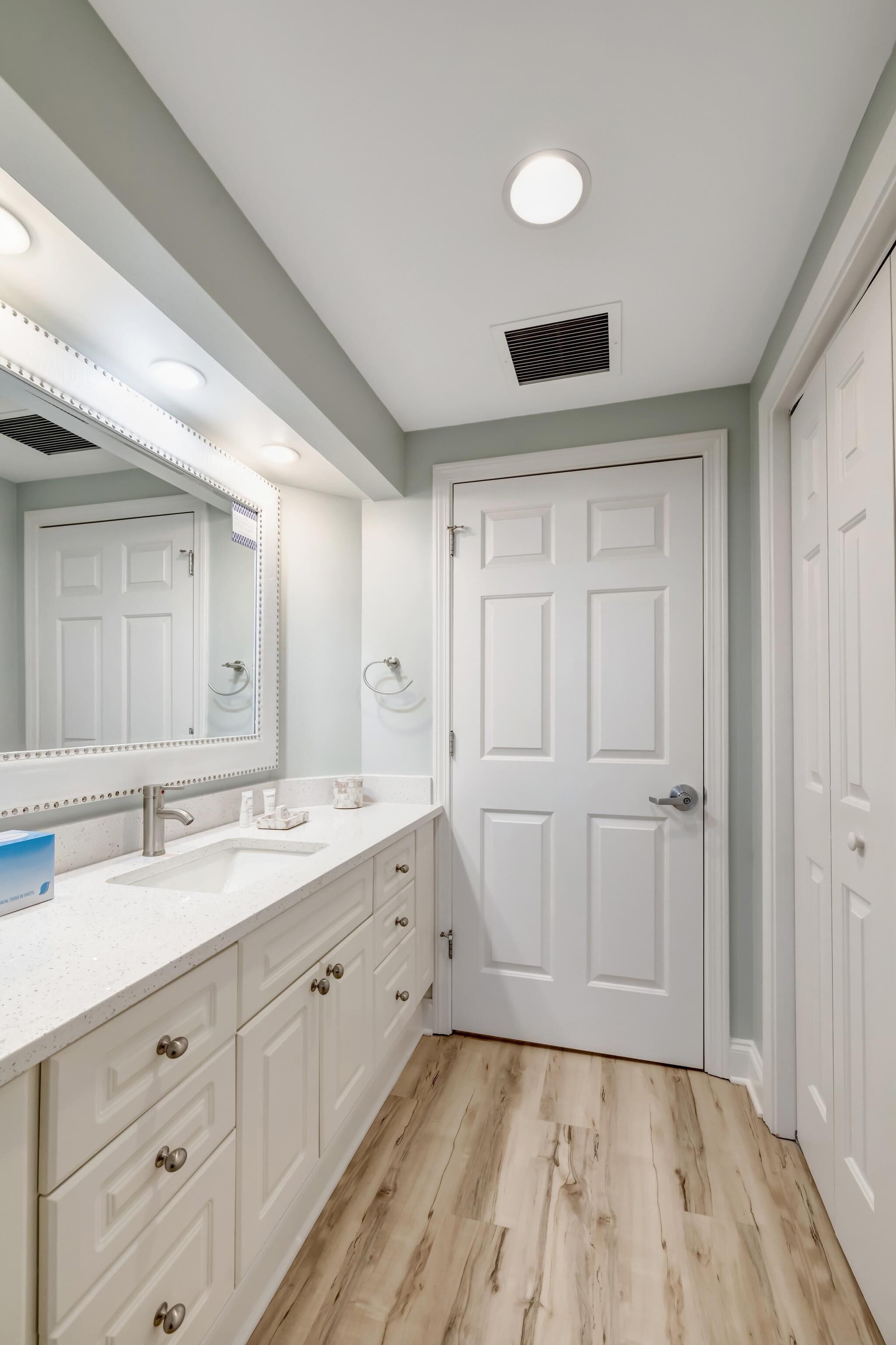 A bathroom with a white vanity, a large mirror, and a white door.