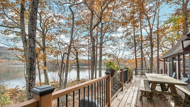A wooden deck with a railing overlooking a lake, surrounded by trees with autumn foliage.