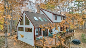 A cabin with a deck, large windows, and a chimney.