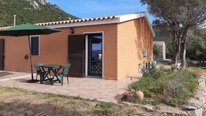 Un piccolo edificio con patio piastrellato, un tavolo e sedie, e un ombrellone verde.