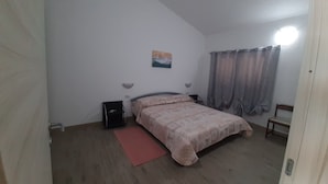 Una camera da letto con un letto, un comodino, una lampada, una sedia, un quadro e una finestra con tende.