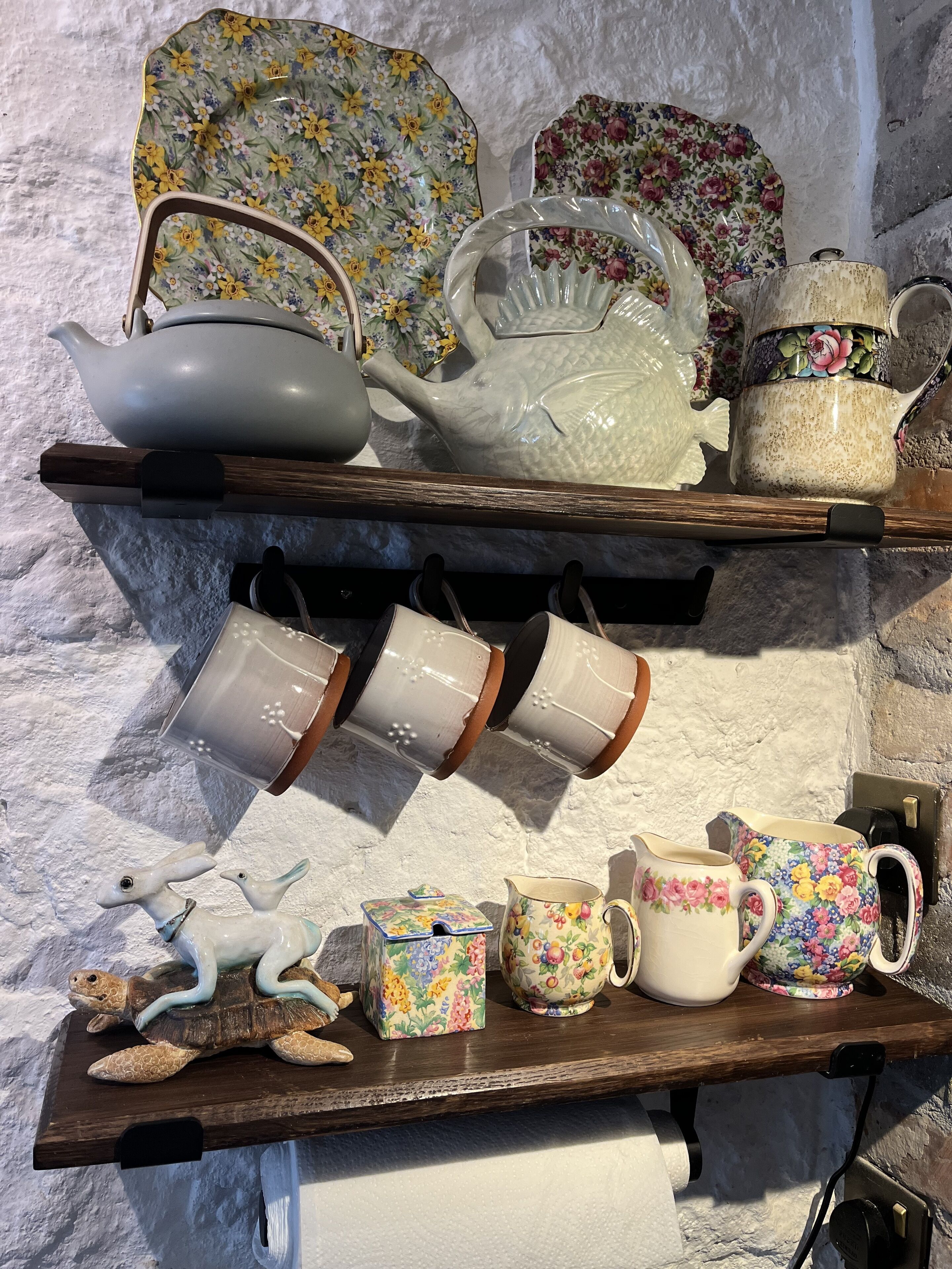 Estant de fusta amb diferents objectes de ceràmica, com a teieres, tasses i una figura decorativa de tortuga.