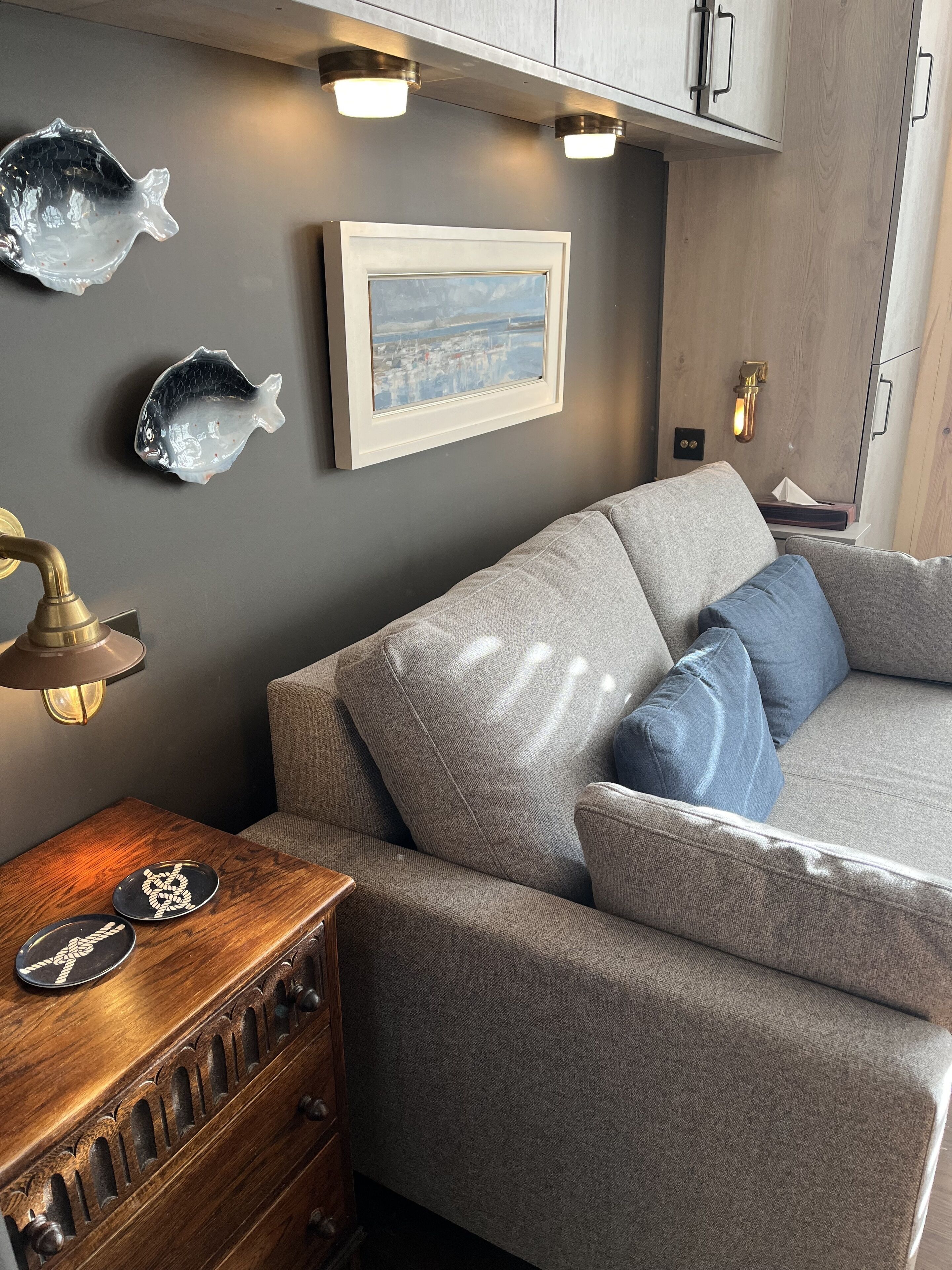 Un espace de vie moderne avec un canapé gris, une table d’appoint en bois et des objets décoratifs en forme de poisson accrochés au mur.
