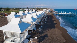 Un hotel frente a la playa con estructuras blancas, un muelle que se adentra en el mar y una vista despejada del océano.