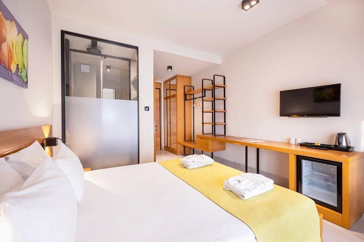 A hotel room with a bed, a desk with a television, a mini-fridge, and a wardrobe.