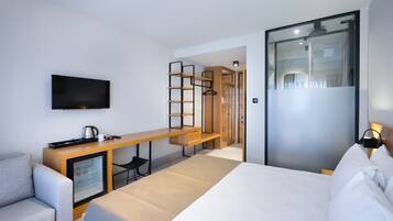 Una habitación de hotel moderna con cama, escritorio con televisor de pantalla plana, mini refrigerador y zona de estar.