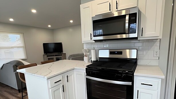 A modern kitchen with white cabinetry, a black stove, and a microwave. - Newly Remodeled Monthly Special!!  2 Bd/1Bath Home! (Parma Heights)