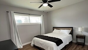 A bedroom with a bed, a ceiling fan, a nightstand, a lamp, and a window with curtains. - Newly Remodeled Monthly Special!!  2 Bd/1Bath Home! (Parma Heights)