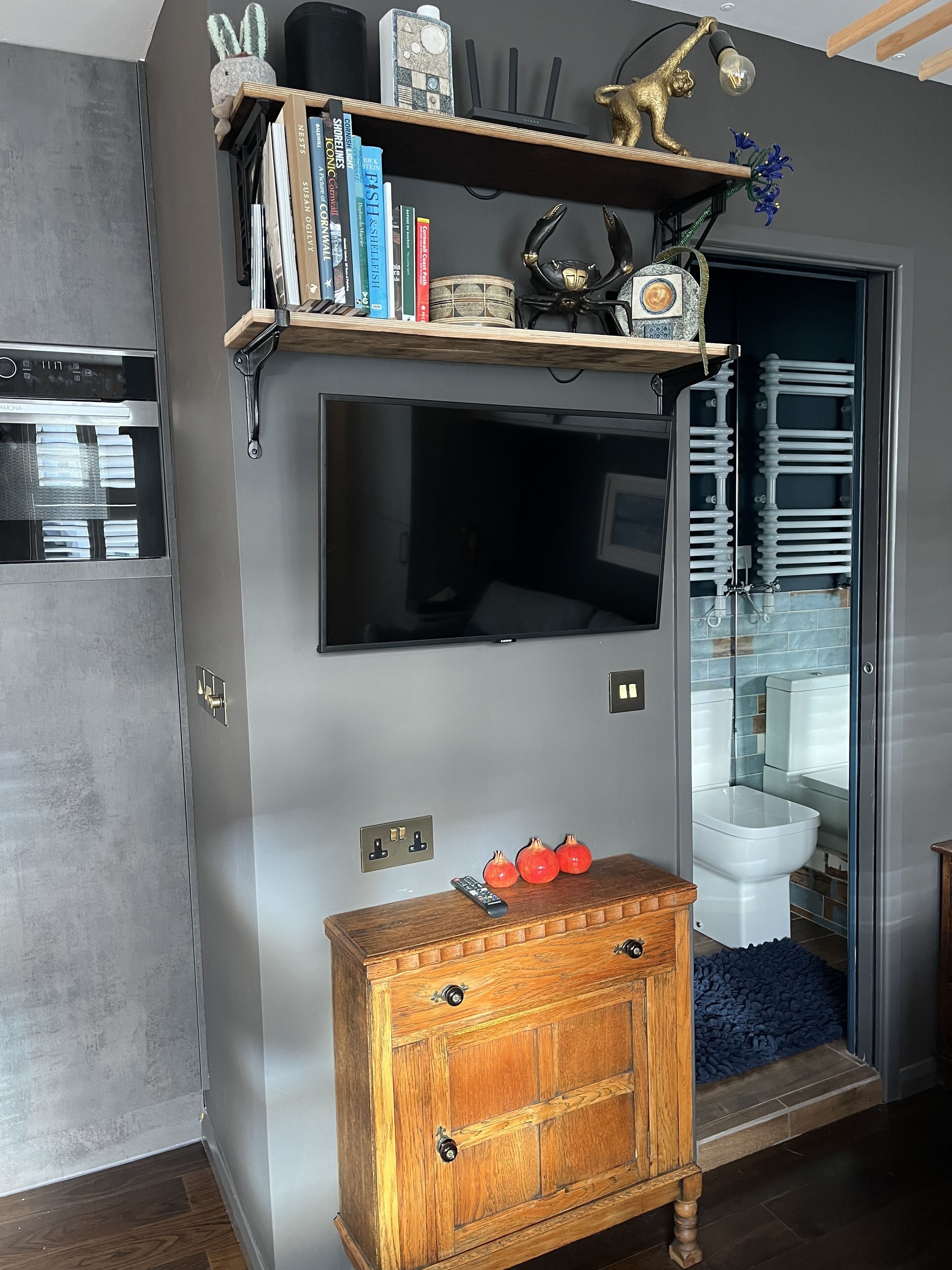 Une salle de bain moderne avec une douche à parois de verre, des toilettes blanches et un meuble-lavabo en bois agrémenté d’une plante en pot.